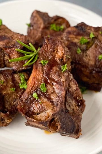 Grilled lamb loin chops on a white plate garnished with fresh parsley and a sprig of rosemary.