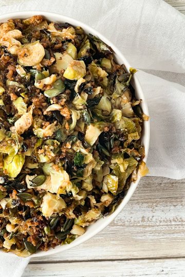 Half a warm Brussels Sprouts Salad in a white bowl on a white cloth and a distressed white wooden table.