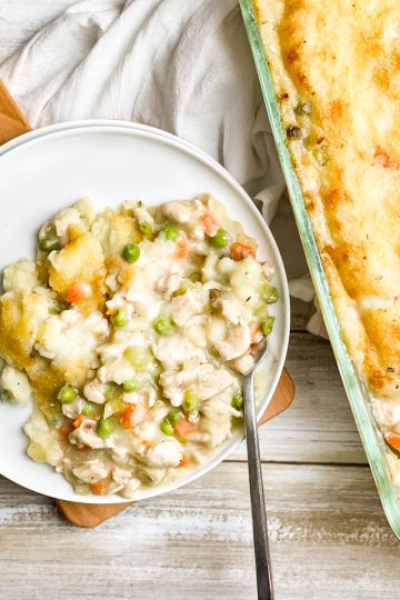 Gluten Free Chicken pot pie on a white plate. A stainless steel fork is in the lower right corner of the plate. The full casserole in the right side.