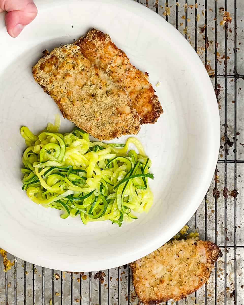 Two gluten free schnitzels on a white plate with zucchini noodles.
