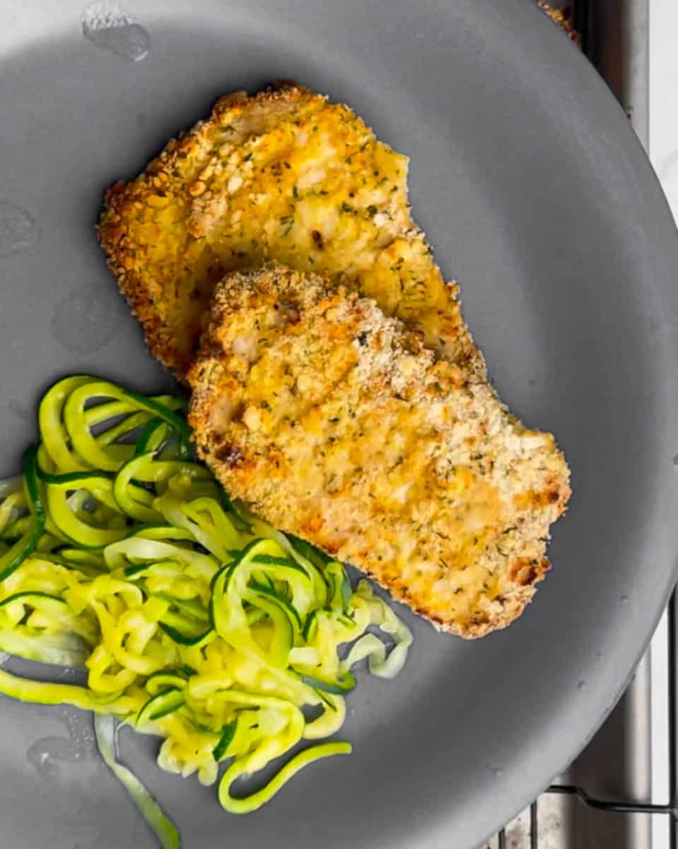 Two gluten free schnitzels on a blue plate with zucchini noodles.