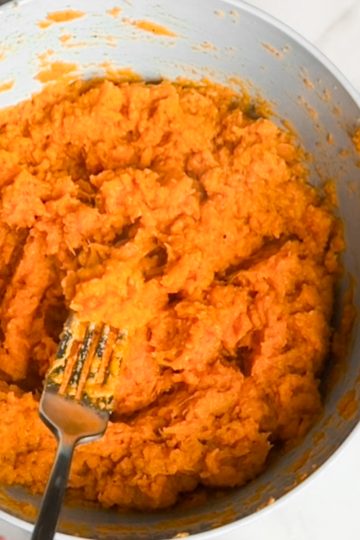 A close up of a fork with savory mashed sweet potatoes over a large bowl of the potatoes.