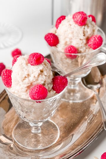 vegan rice pudding topped with raspberried in crystal glasses on a silver tray.