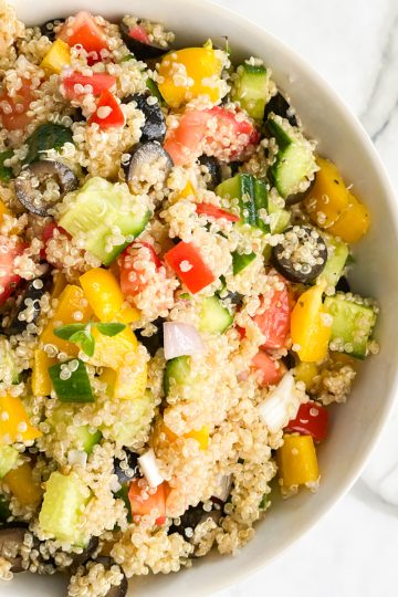 A close up of half of a Mediterranean quinoa salad in a white bowl.